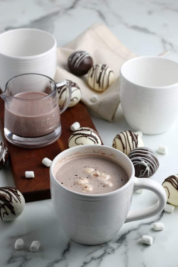 a white ceramic cup filled with hot chocolate with the hot cocoa bombs next to them