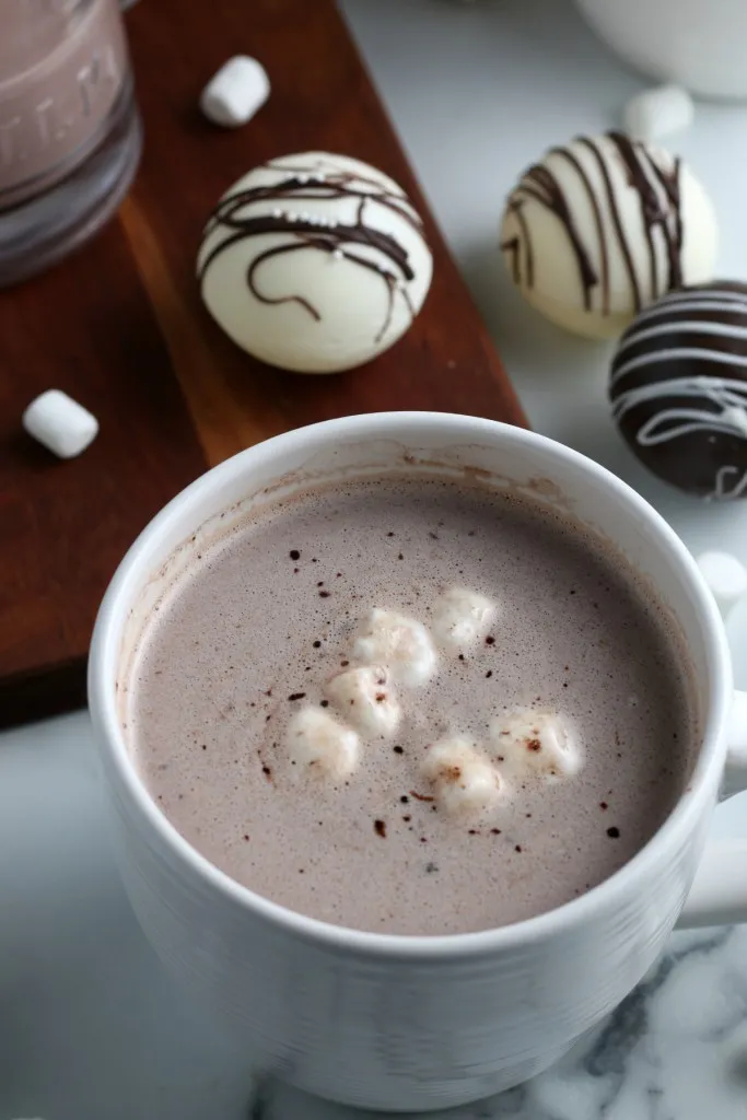 hot chocolate bombs in a white coffee cup on a wooden board