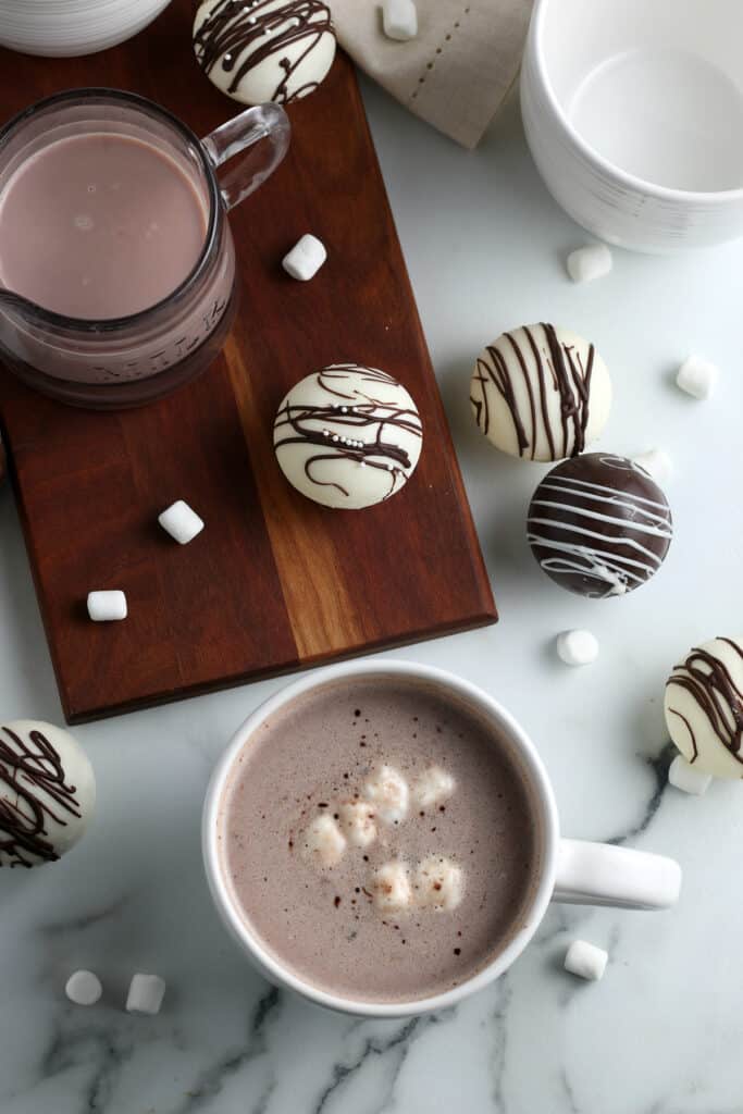 overhead shot of multiple hot chocolate bombs on a wooden board with mini marshmallows sprinkled around
