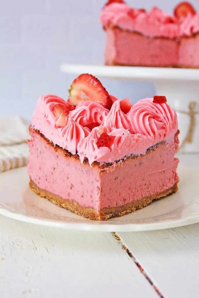 ari fryer strawberry cheesecake slice on a white plate next to a cake stand with the remaining cheesecake on it