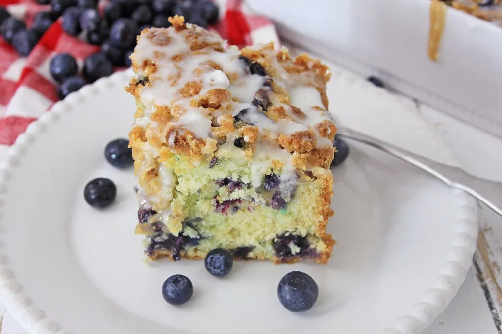 side view of a slice of a blueberry crumb coffee cake on a white ceramic plate