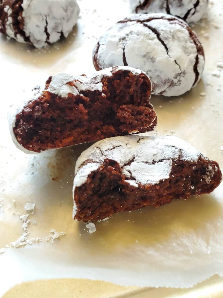 a close up shot of a chocolate crinkle cookie broken in a half on parchment paper