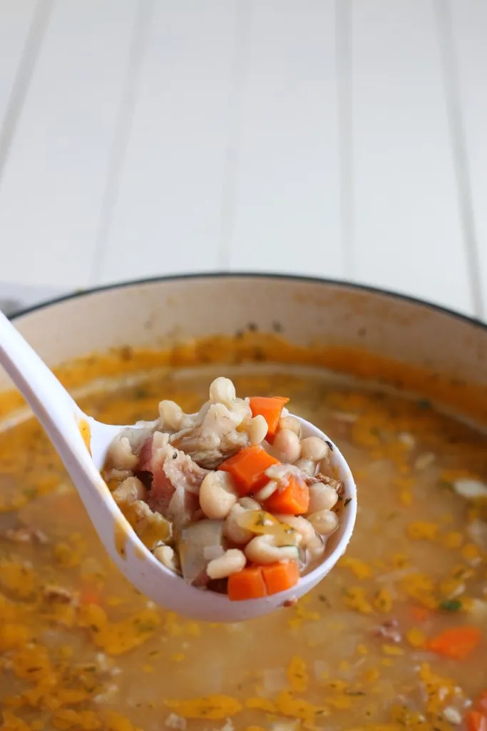 Ladle lifting creamy white bean and ham soup from a Dutch oven