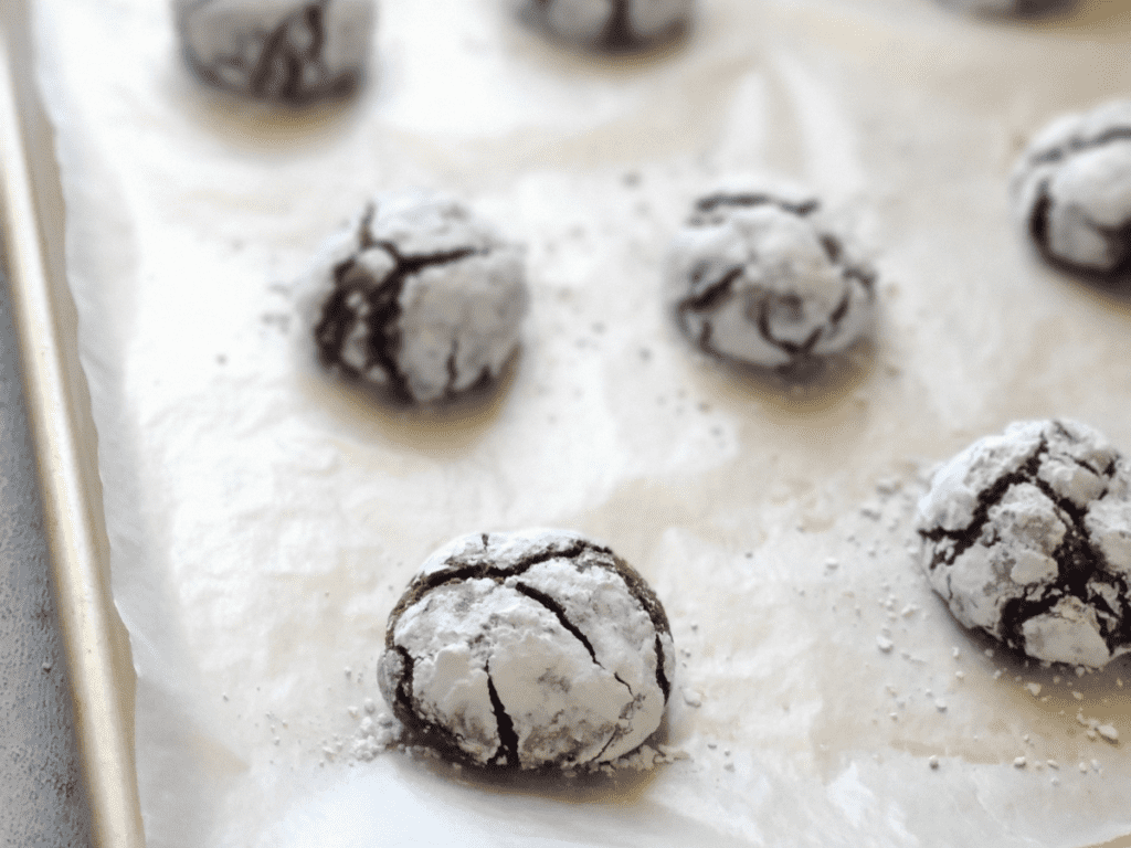 a tray of chocolate crinkle cookies on a parchment paper lined co0okie sheet