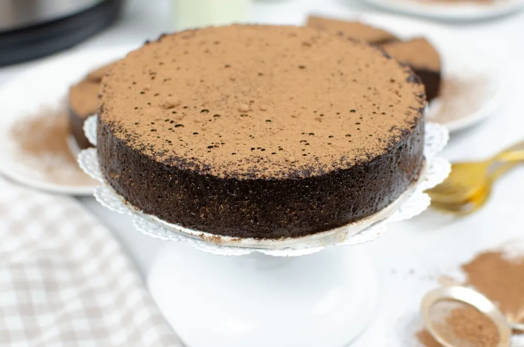 a dense rich flourless chocolate cake on a ceramic cake holder dusted with cocoa on top