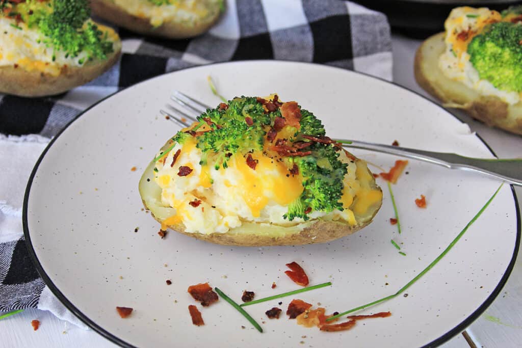 horizontal photo of a backed potato topped with broccoli, bacon, and cheese on a stone plate