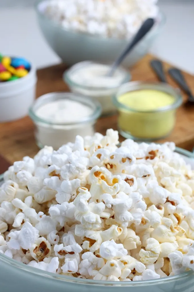 a bowl of freshly made popcorn with bowls of candy in background