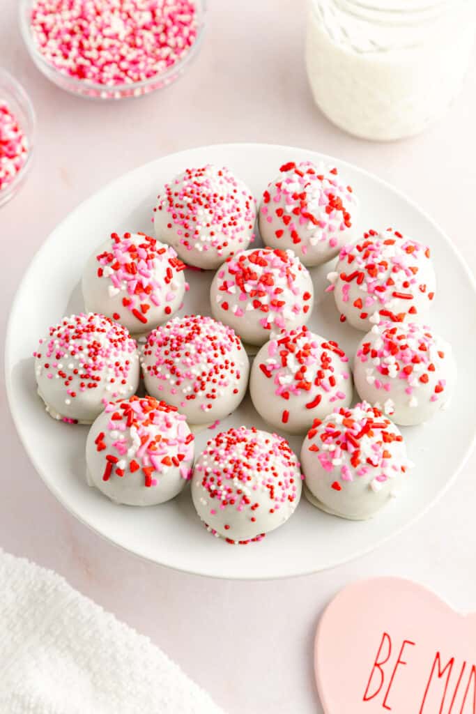 red velvet balls covered in white chocolate on a white plate with red, pink, and white sprinkles