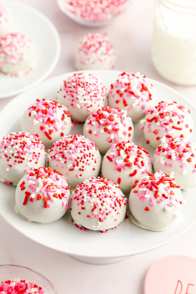 side view of white chocolate covered red velvet cake mix balls with red, pink and purple heart shaped and normal sprinkles