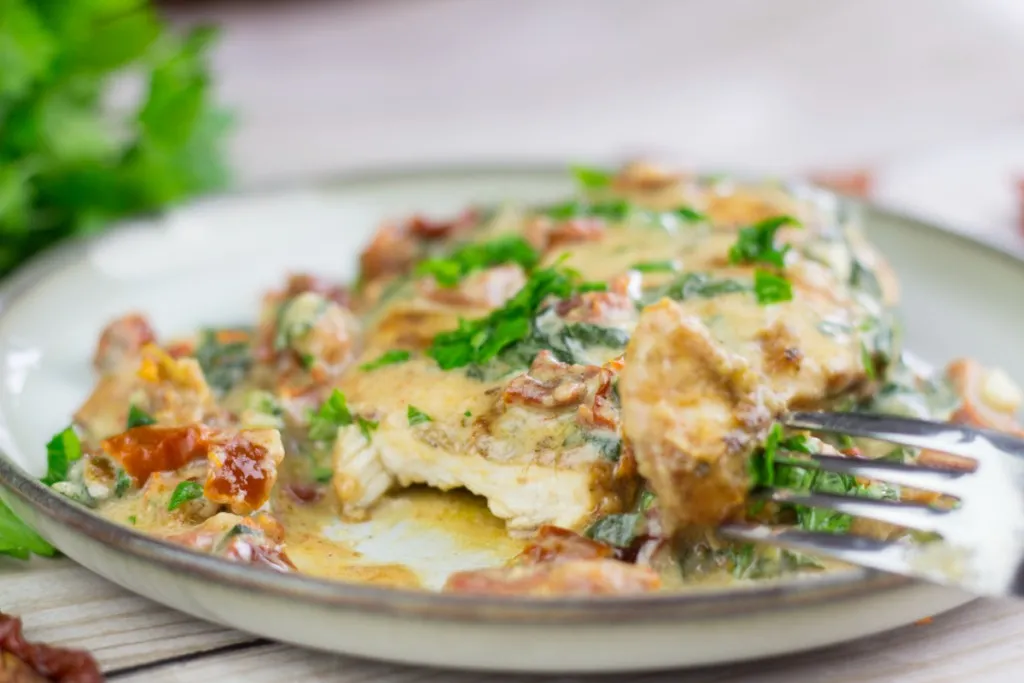 A fork full of tuscan chicken with a cream sauce