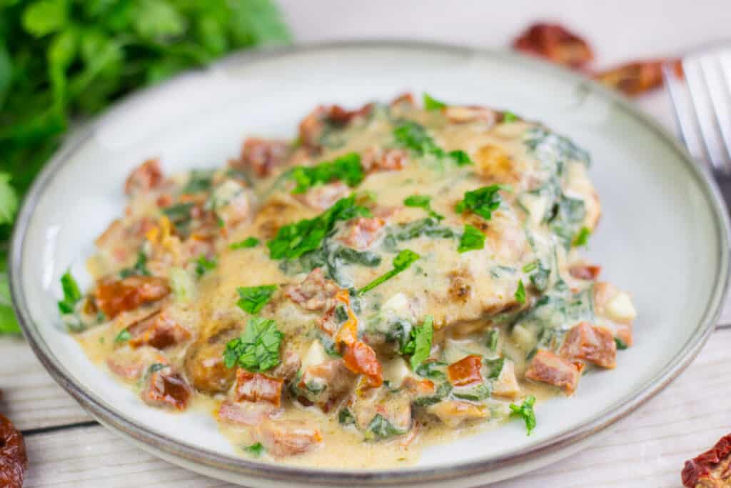 a piece a tuscan chicken with a cream sauce with sun dried tomatoes and parsley