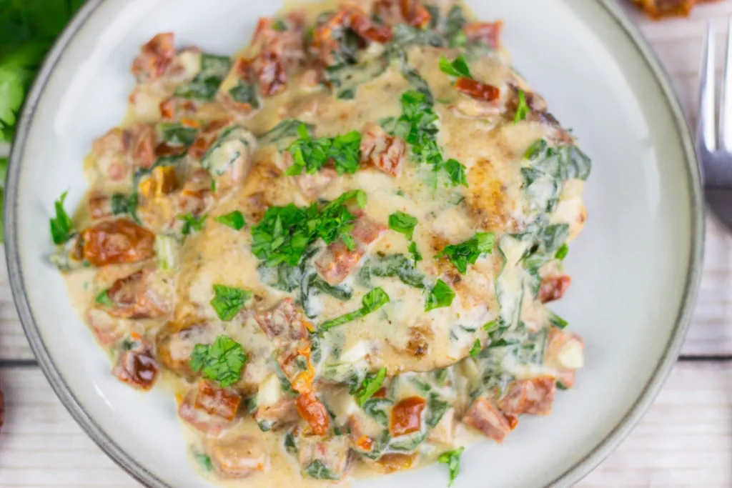overhead view of a creamy tuscan chicken recipe on a ceramic plate with parsley on top