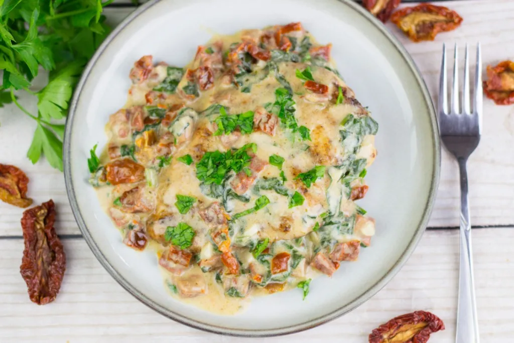 chicken with a creamy tuscan sauce with sun dried tomatoes with a fork on a ceramic plate