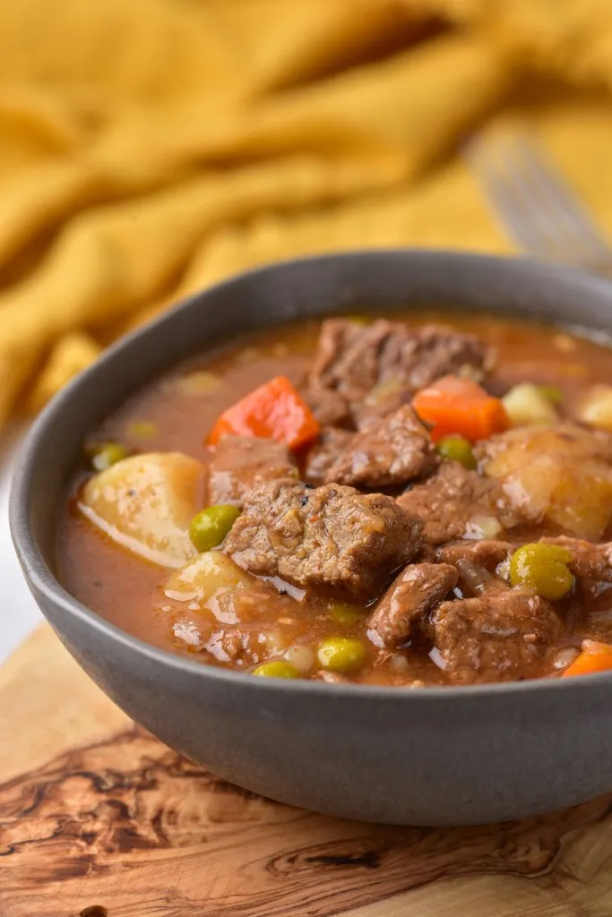 side view of a pot of fresh made instant pot beef stew in a grey stone colored bowl on a wooden cutting board