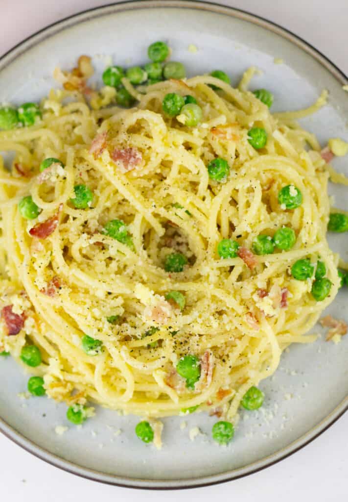 overhead view of a pile of pasta carbonara on a stone colored ceramic plate