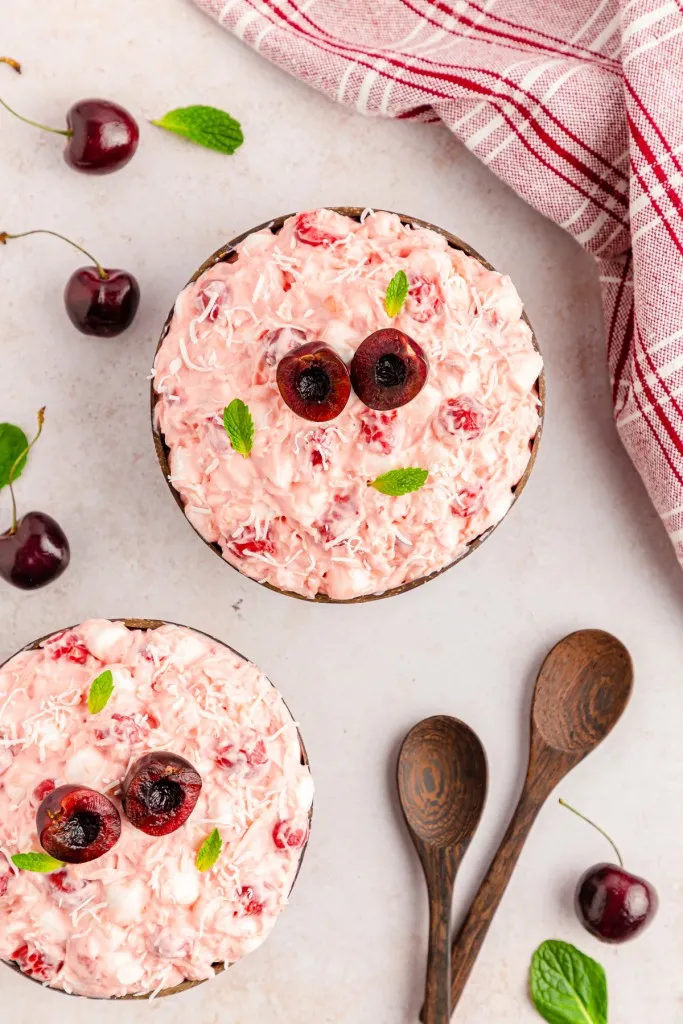 2 hand carved dark stained wooden bowls filled with homemade cherry fluff salad and 2 dark stained wooden flat spoons next to them