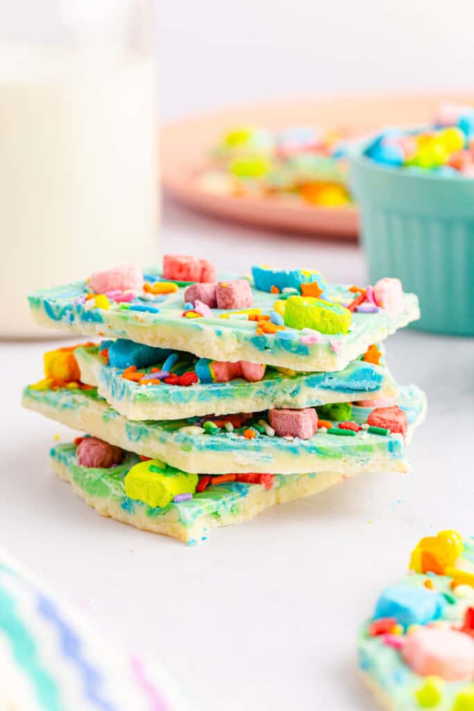 side view of stacked rainbow lucky charms bark with a glass of milk in the background