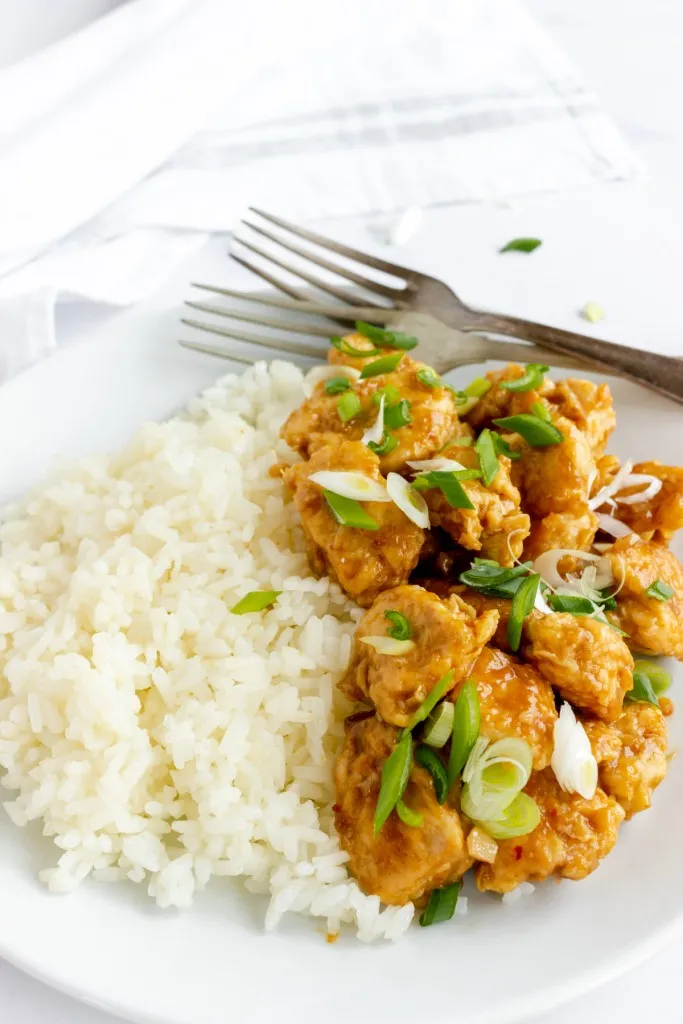 side view of homemade copycat panda express orange chicken with cooked rice and diced green onions.