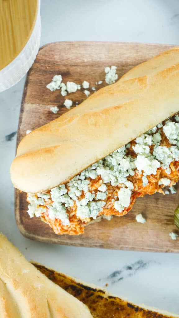 slow cooker buffalo chicken on a sub with crumbled bleu cheese on a wooden board