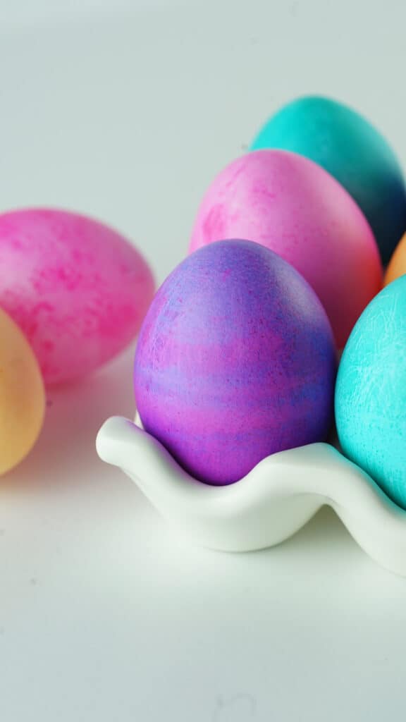 close view of beautiful hand made dyed easter eggs of different colors in a white ceramic egg crate