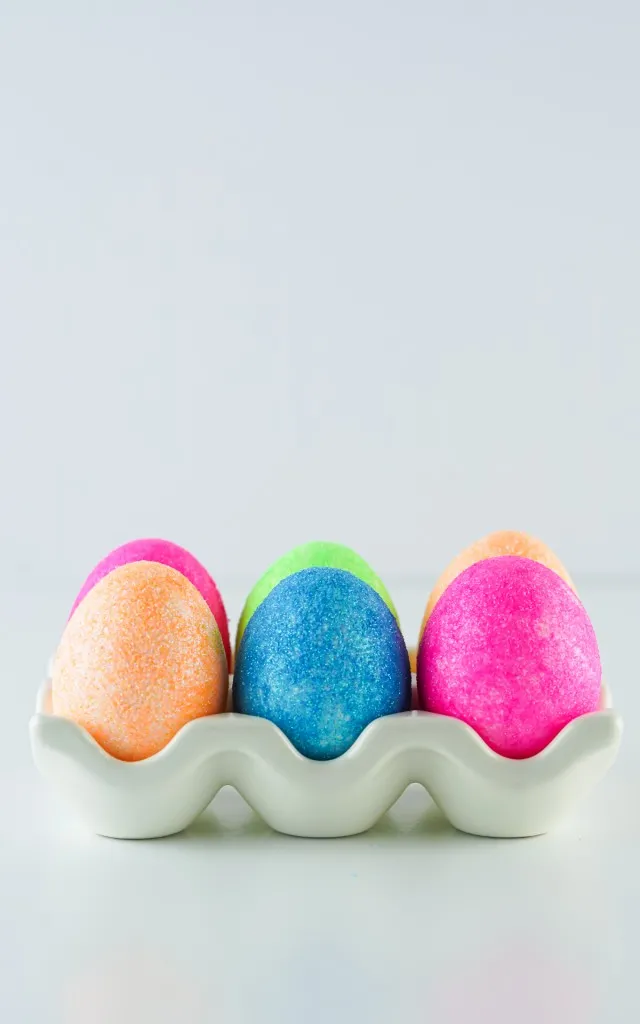 main hero image of glittered covered easter eggs sitting in a white ceramic egg holder