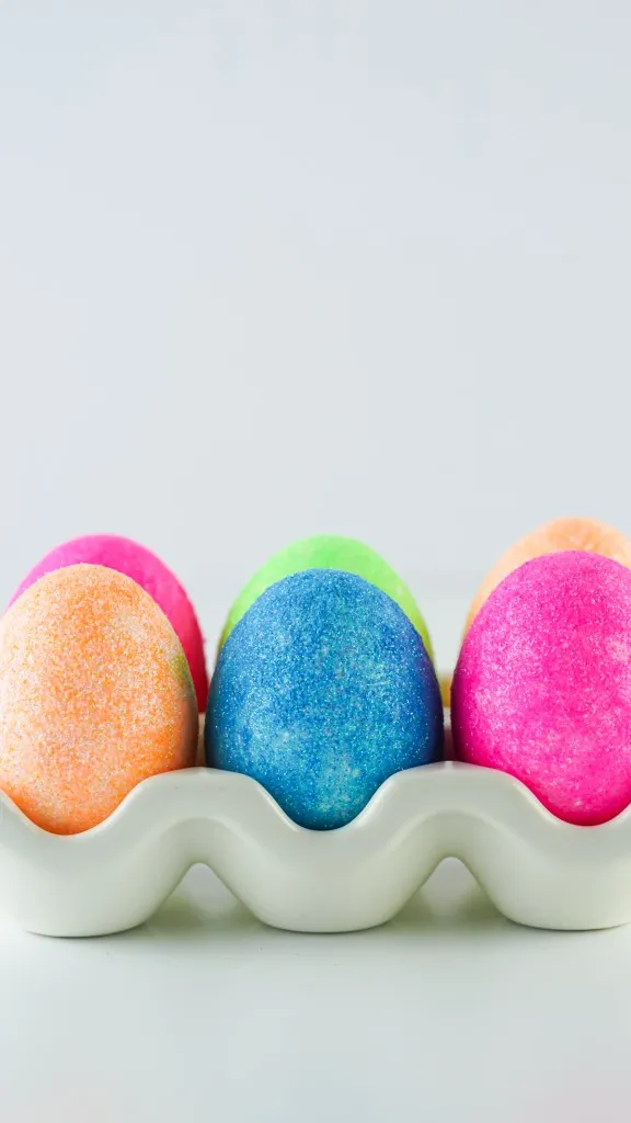 side view of orange, blue, and pink colored glitter easter eggs in a ceramic egg container