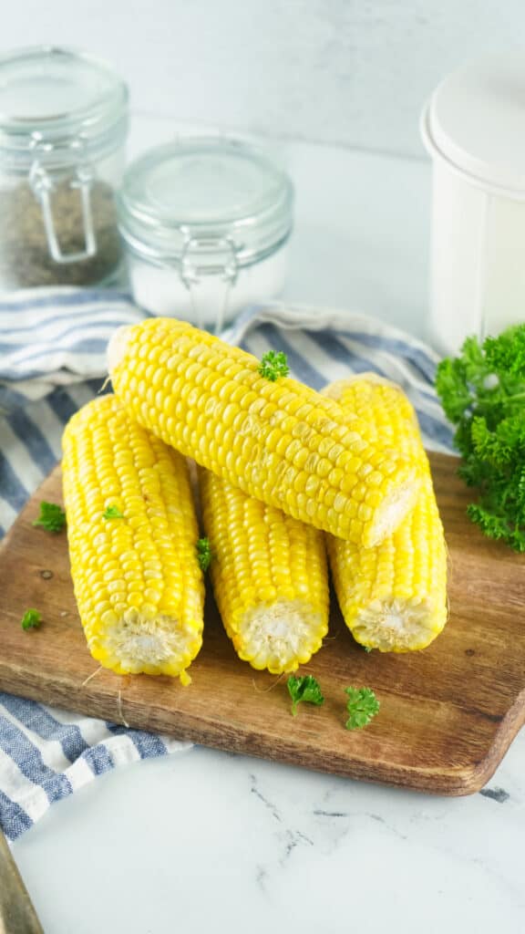 wooden cutting board of corn on the cob resting on it with fresh parsley