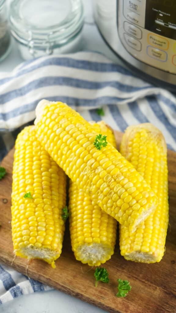instant pot corn on the cob on a wooden cutting board sprinkled with fresh parsley to garnish