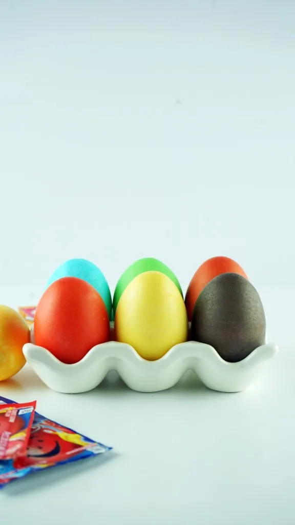 side view of kool aid dyed eggs sitting in a white ceramic egg holder.