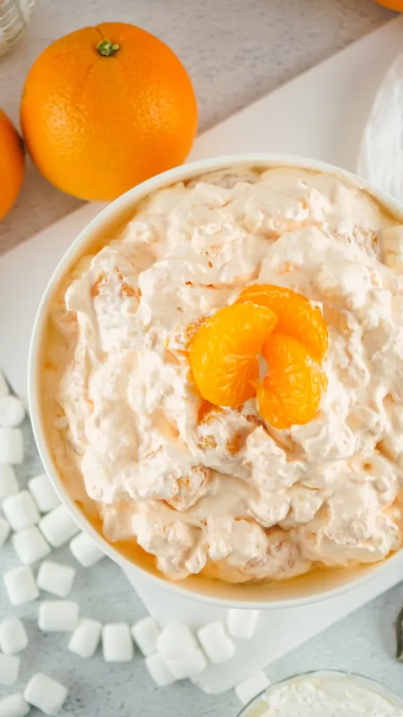 overhead view of orange fluff salad topped with mandarin orange segments in a white bowl