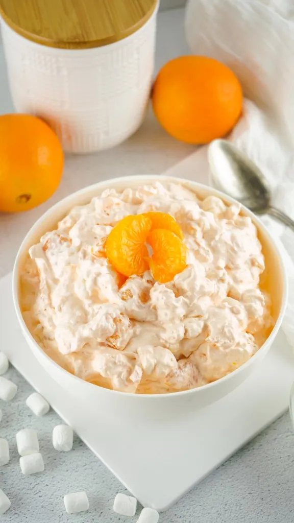 best ever orange fluff salad in a white bowl on a square plate with mini marshmallows