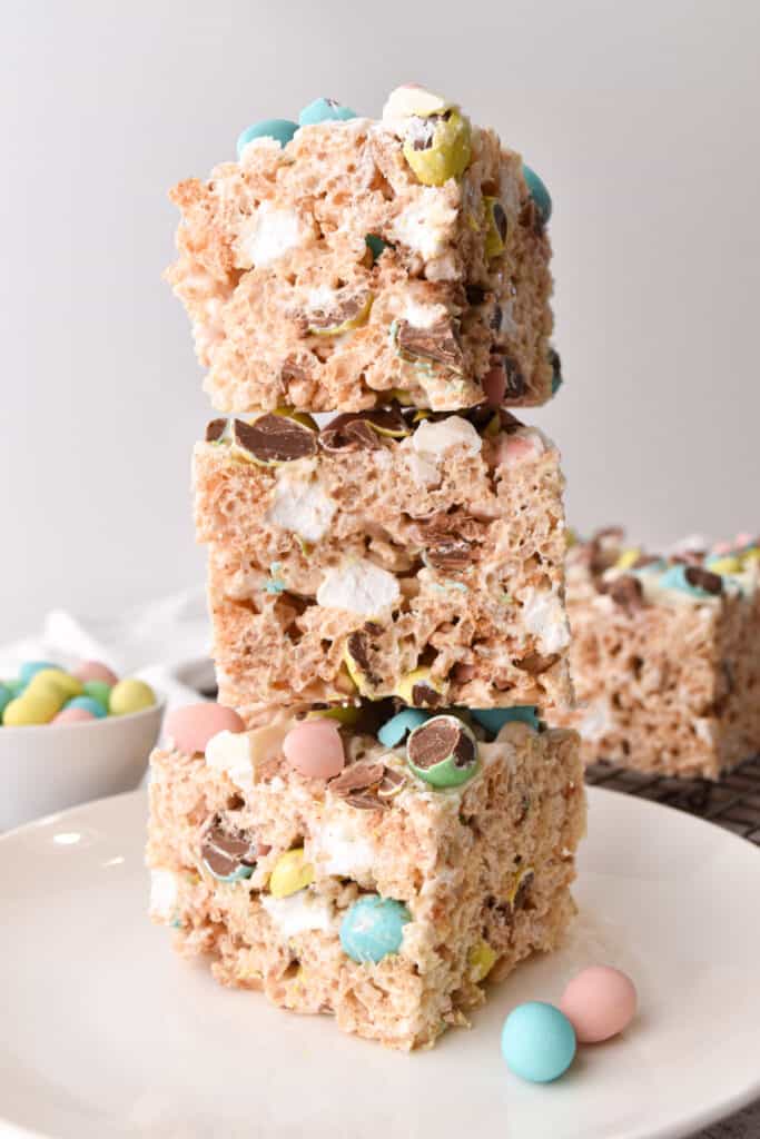 Easter rice krispies treats stacked on top of each other with a bowl of mini chocolate cadbury eggs