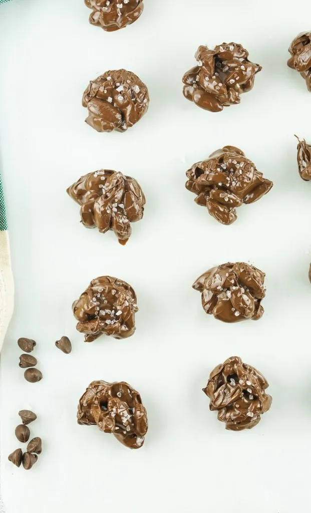 overhead shot of chocolate almond clusters dusted with sea salt on a piece of parchment paper and chocolate chips sprinkled around