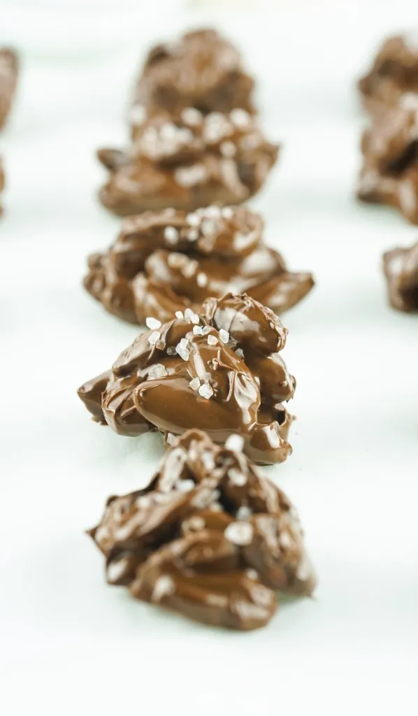 a closeup view of chocolate almond clusters dusted with sea salt on a piece of parchment paper