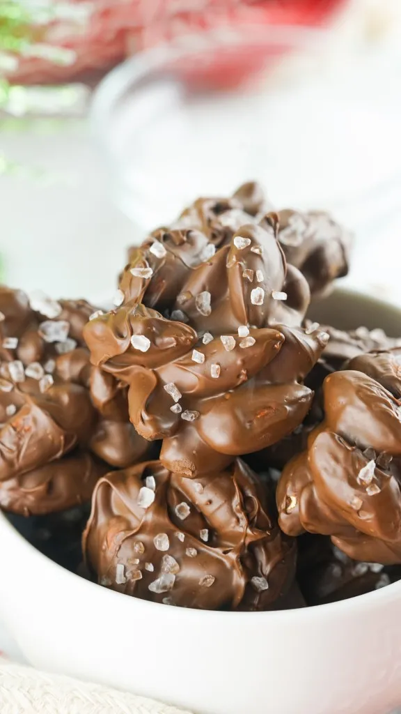 a close up view of a white ceramic bowl filled with sea salt chocolate almond clusters