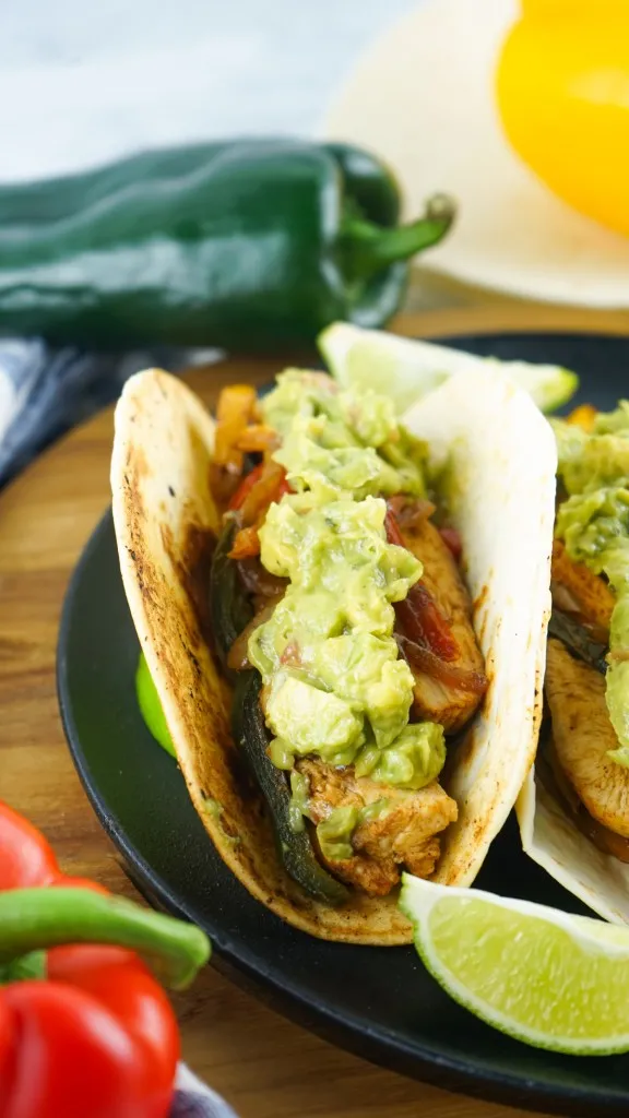 Homemade avocado salsa on easy to make skillet chicken fajitas recipe with poblano peppers in the background