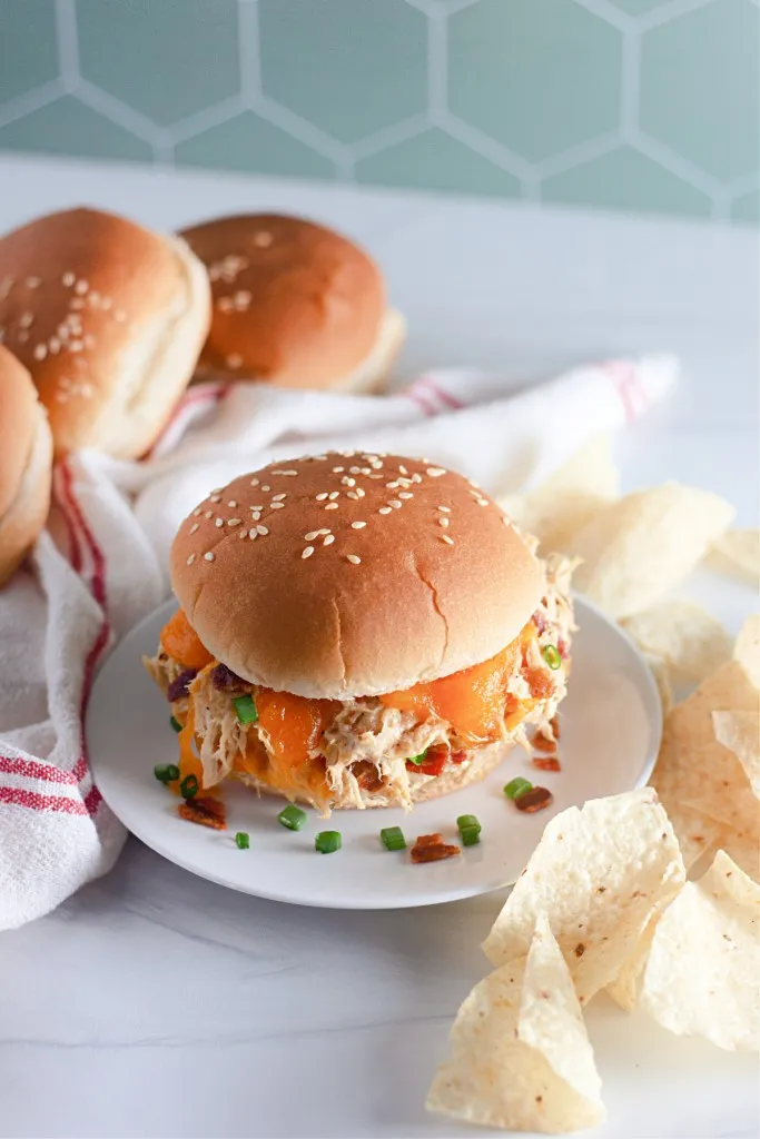 slow cooker crack chicken sandwich on a white plate with chips in the background