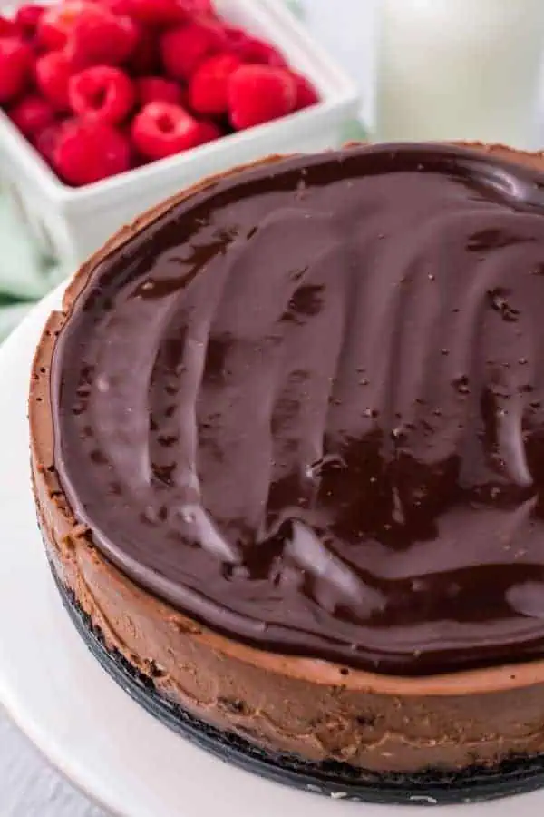 a chocolate cheesecake with a layer of chocolate ganache fresh raspberries in background
