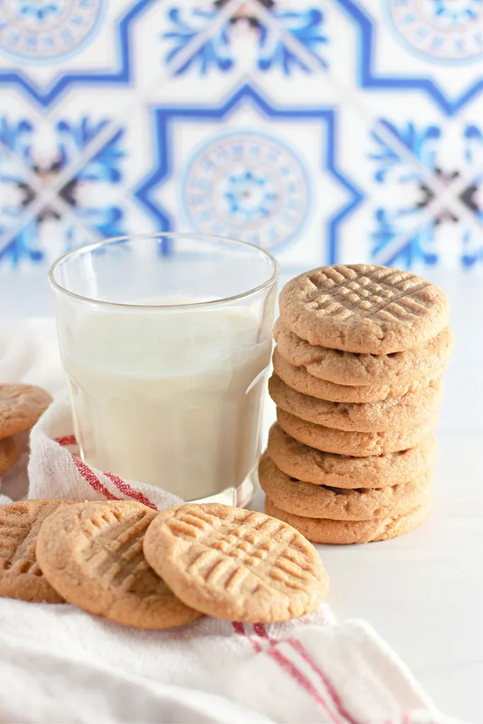 3 ingredient peanut butter cookies in front a blue tile background with a glass of milk