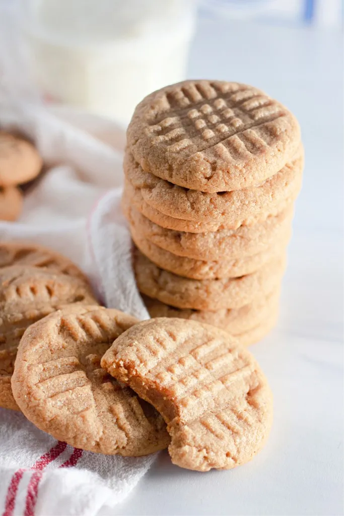 peanut butter cookies stacked on a each other with a bite taken out of one cookie standing next to a glass of milk