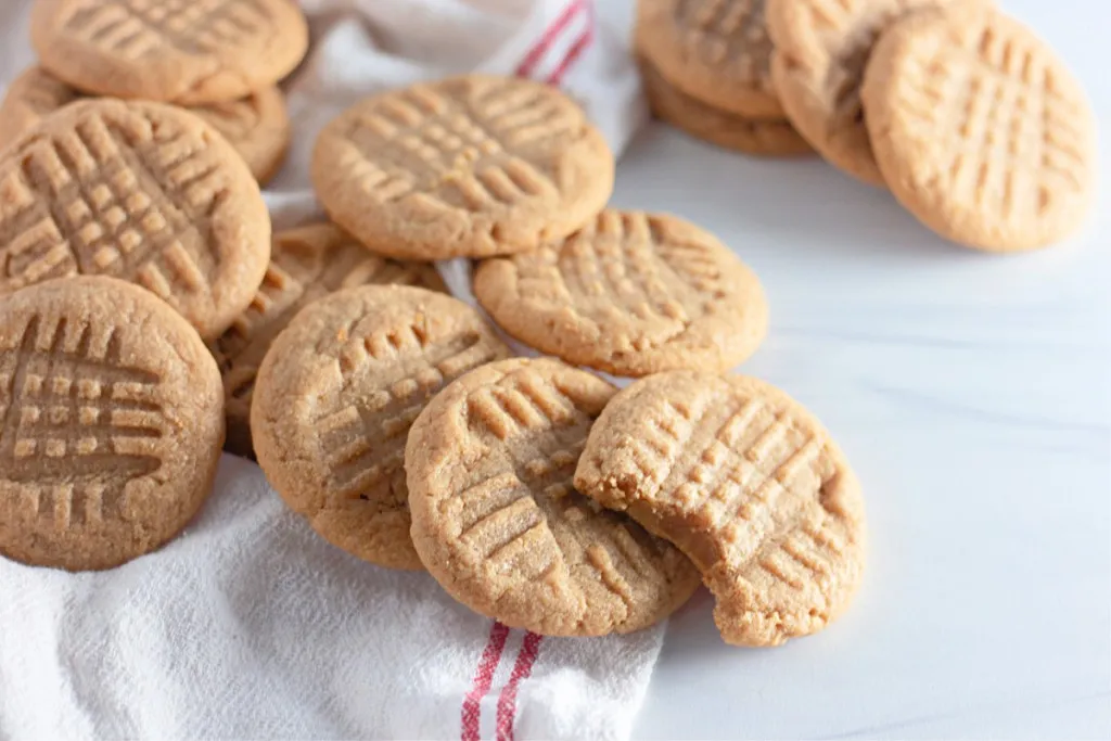 scattered peanut butter cookies on a white and red striped linen towel