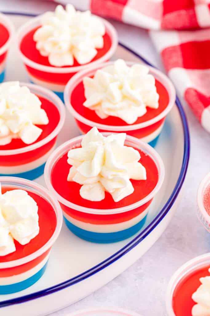 close up view and red, white, and blue jello shots with a dollop of whipped cream on a white plate