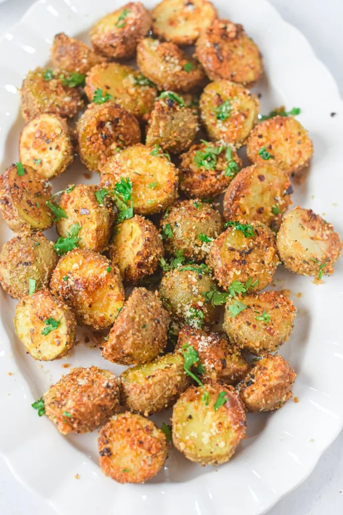 Overhead view of air fryer parmesan potatoes on a white serving plate.