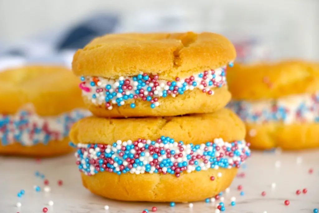 Close up of two stacked air fryer sugar cookie whoopie pies, two sugar cookie whoopie pies in the background.