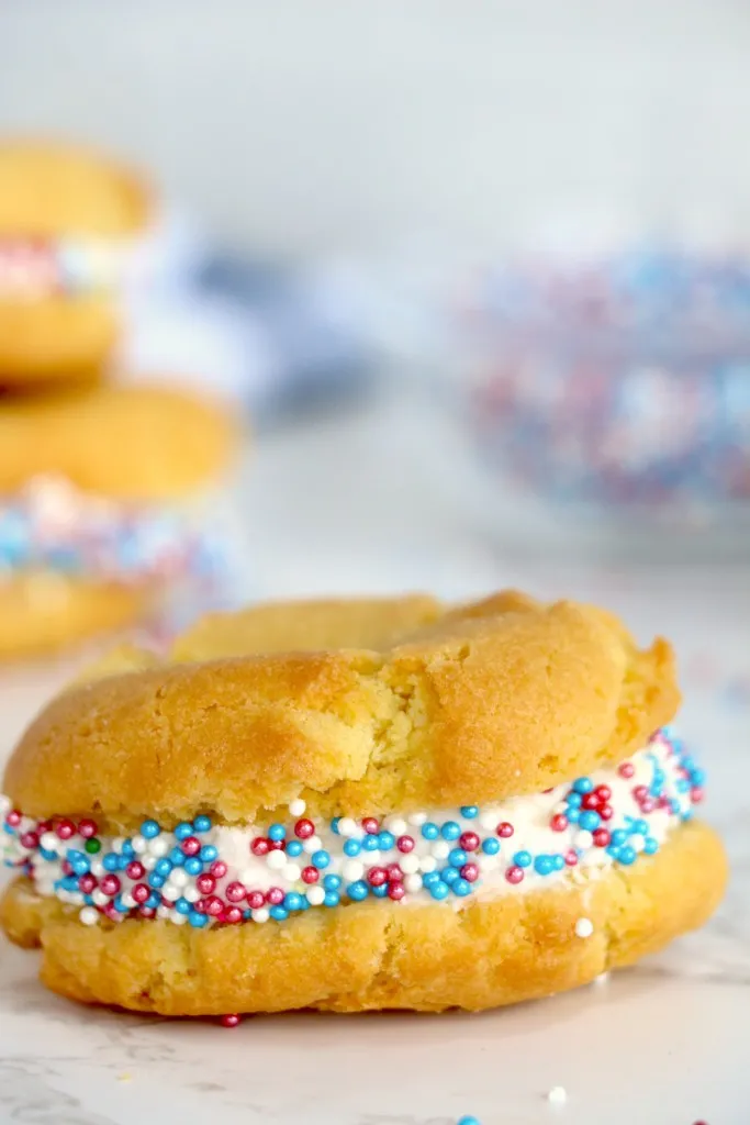 Single air fryer sugar cookie whoopie pie with more sugar cookie whoopie pies in the background.