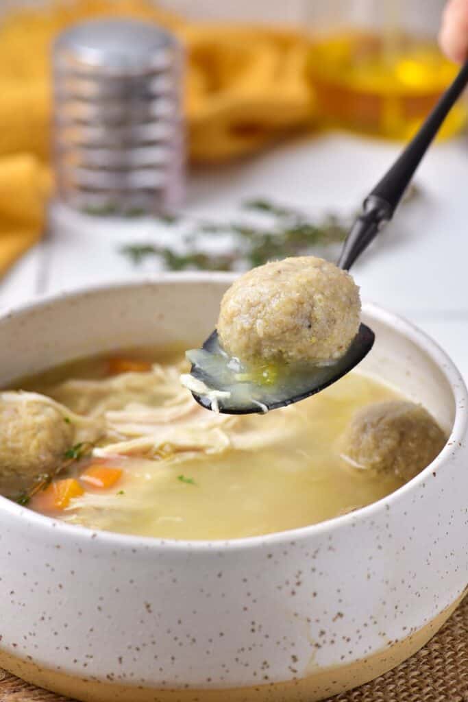 Bowl of Matzo ball soup with a metal spoon holding a chicken meatball.