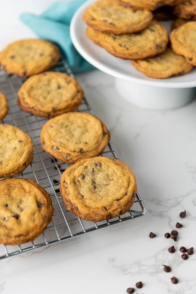 Wire cooling rack with mini chocolate chips, white cake stand with mini chocolate chips, on a marble countertop. 