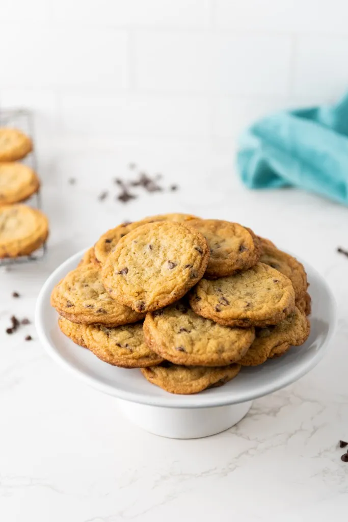 Mini chocolate chips on a white cake stand, mini chocolate chip cookies on a wire rack.