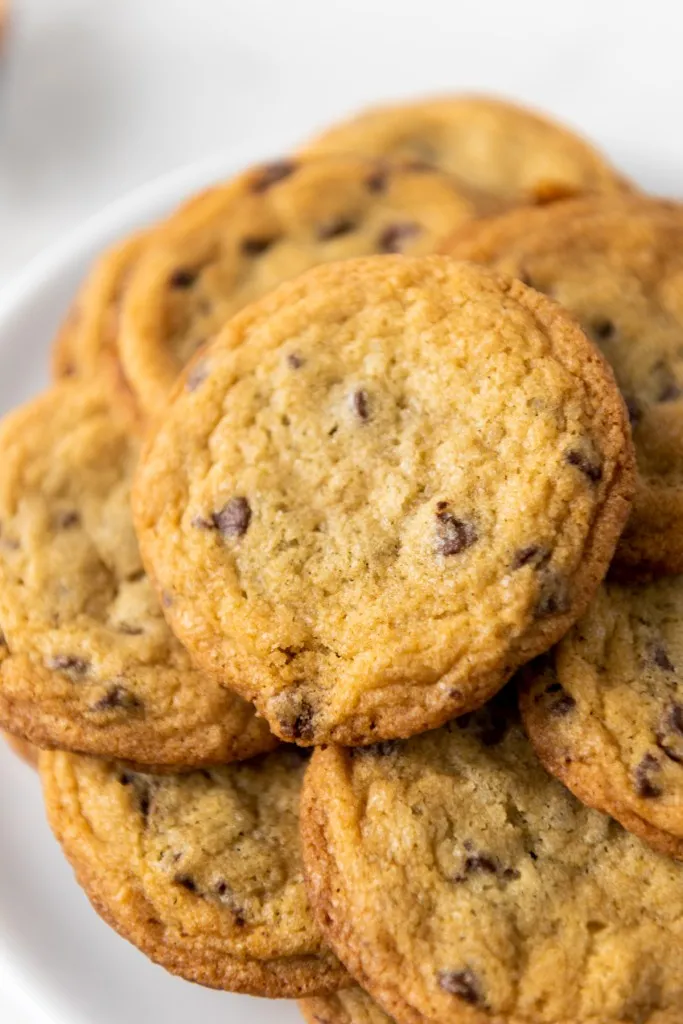 Pile of mini chocolate chip cookies on a white cake stand.