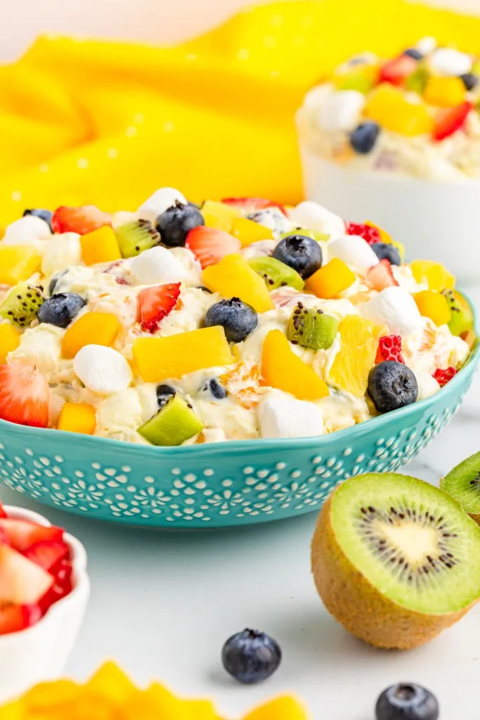 Bowl of tropical fruit marshmallow fluff, fresh fruit on a white kitchen countertop.